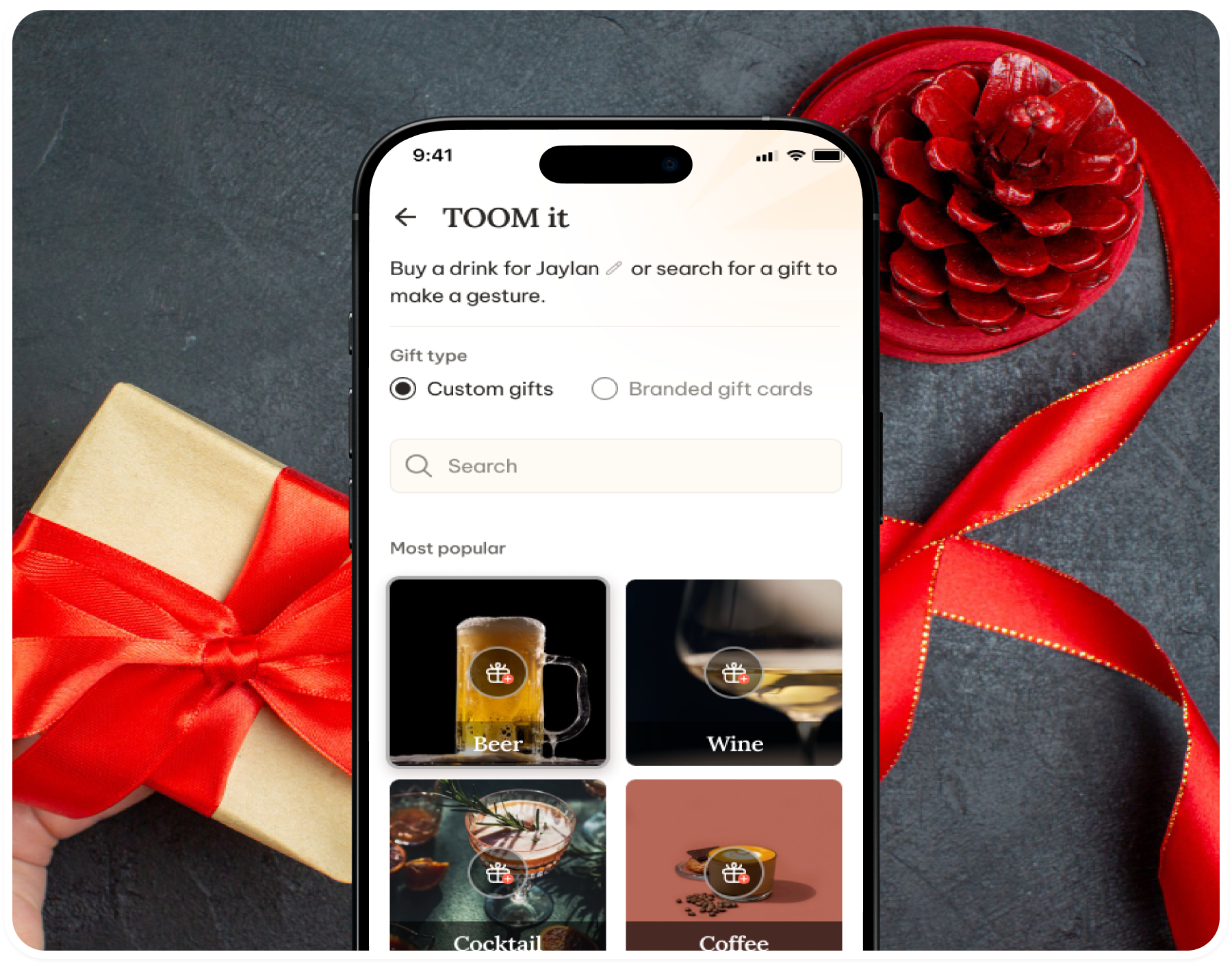 The custom gift screen on a phone next to a red ribbon and pine cone
